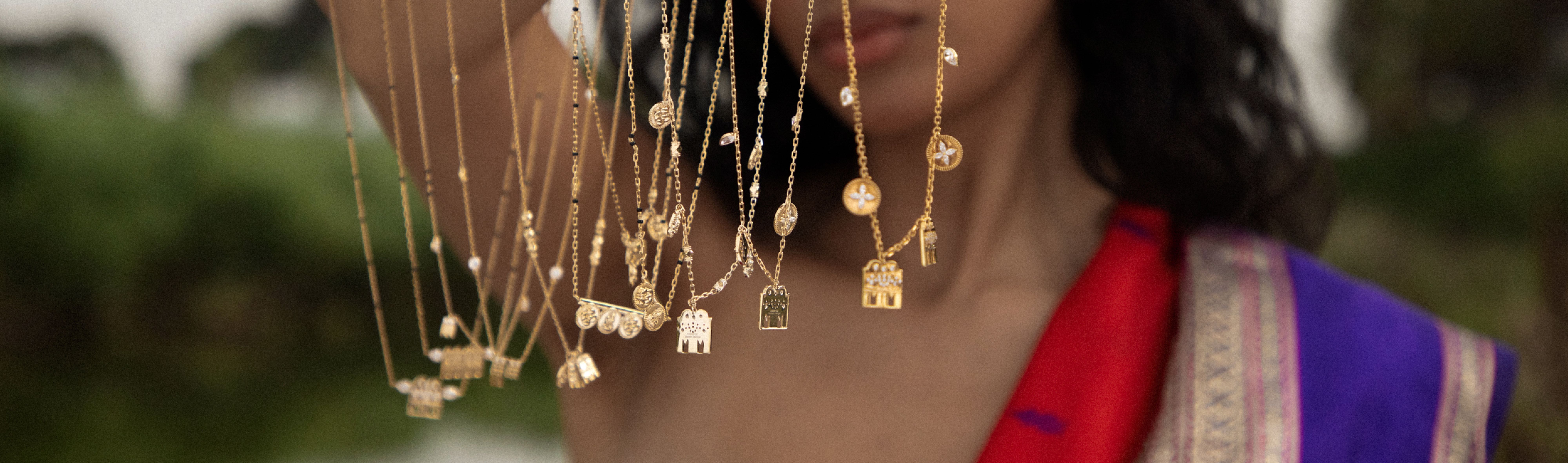 Modern Mangal gold charm pendants on delicate chains held up by a model in a red and purple saree